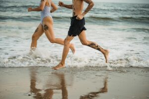 Energetic couple jogging along the beach with waves splashing against the shore.